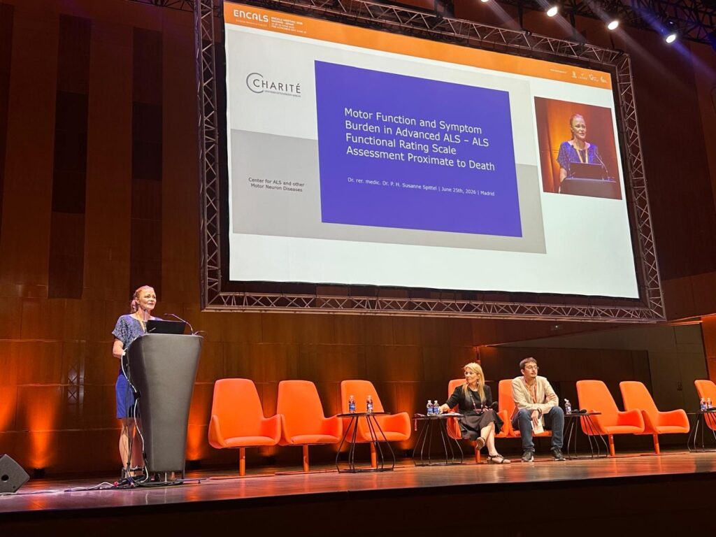 APST_Newsletter 2026_Ambulanzpartner Forschung beim ENCALS Meeting_Bild 1_20260708 Female speaker at a podium presenting on a large screen; panelists seated in orange chairs on stage.
