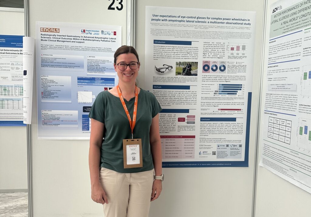 APST_Newsletter 2026_Ambulanzpartner Forschung beim ENCALS Meeting_Bild 4_20260708 Smiling woman standing in front of scientific posters at a conference, wearing a green top and orange lanyard badge.